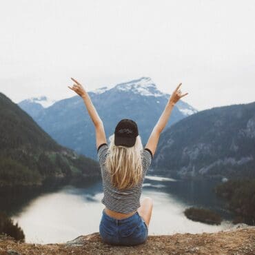 woman sitting on cliff raising both hands